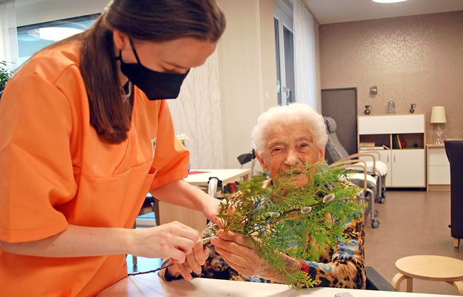 Seniorin im Rollstuhl hält Palmzweige Pflegekraft hilft