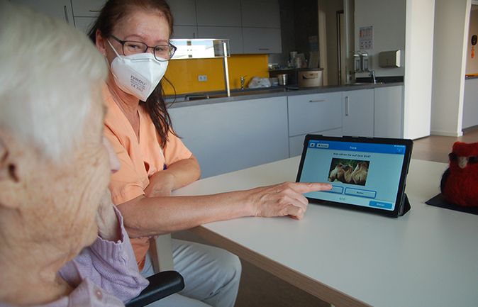 Pflegekraft zeigt Tablet mit Quiz an ältere Person
