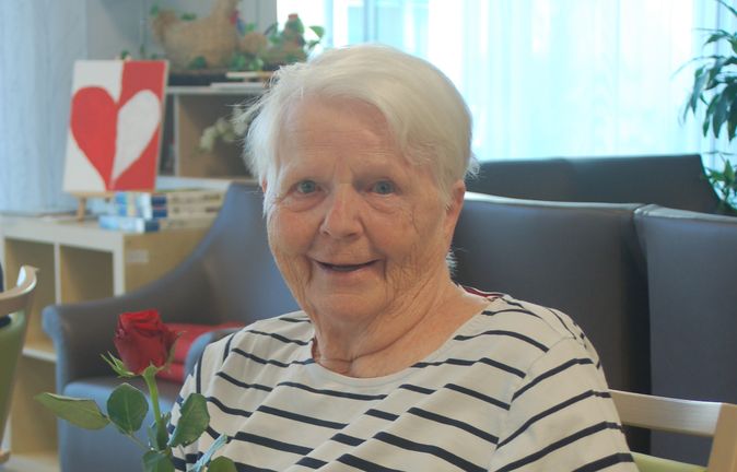 Ältere Frau sitzt lächelnd mit roter Rose zum Muttertag