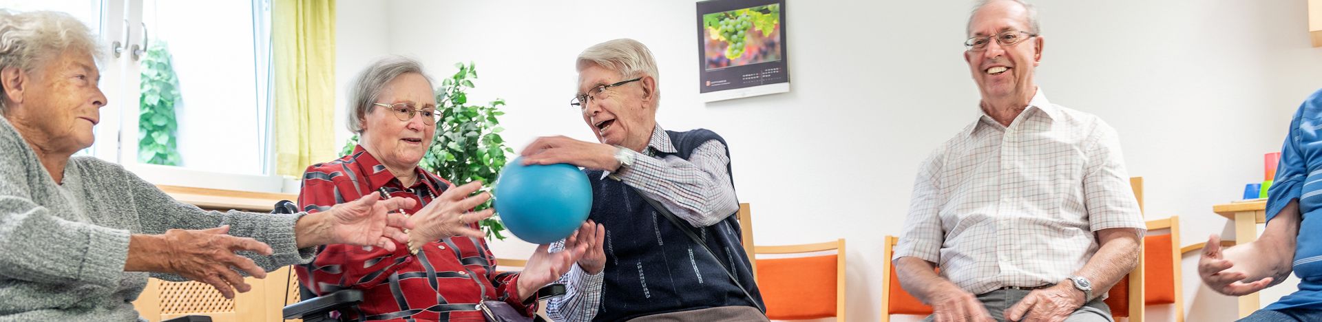 Ältere Menschen im Sitzkreis geben sich einen blauen Ball