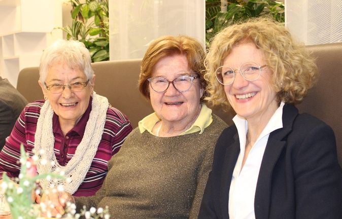 Drei lächelnde Frauen sitzen nebeneinander an einem Tisch