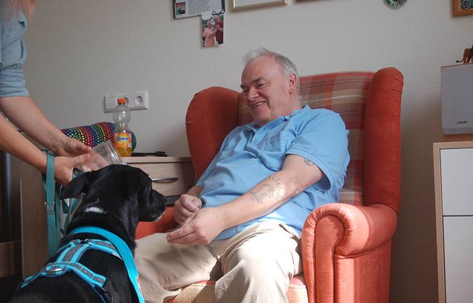 Älterer Mann lächelt im Sessel beim Besuchshund