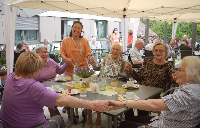 Seniorinnen und Pflegekraft halten Händchen bei Kaffeetafel im Freien